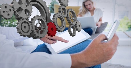 Composition of connected 3d cogs over man and woman in office using tablet, smartphone and laptop