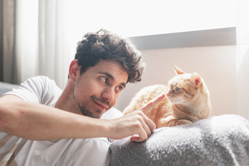 young man under the window strokes the muzzle of a brown tabby cat. close up