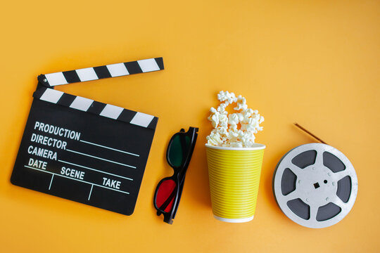 clapperboard, cinema glasses, film strip and popcorn bucket on yellow background. movie night concept. flatlay. top view. copy space