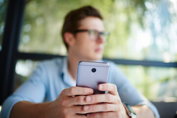 Blurred male blogger holding modern cellphone technology in hands creating content text and publication during leisure pastime, unrecognizable man with digital mobile gadget phoning indoors