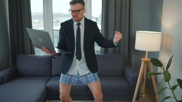 Caucasian man dressed in a jacket and underwear using laptop to make a video call from home in a modern apartment. Remote work during a pandemic