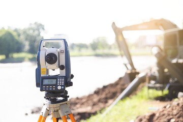 Theodolite in construction.To find accurate level values. In the background is the water pump and backhoe . - obrazy, fototapety, plakaty