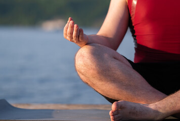 A young man practices yoga on the river bank. The concept of weight loss and sports in nature.