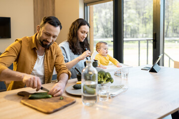 Young happy family with a one year baby boy during a lunch time at home. Concept of healthy vegan eating and happy parenting