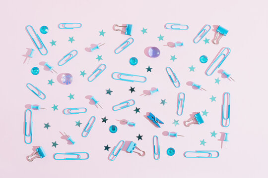 Modern pattern made of light blue clip and pin set, with blue stars. On brite pink background. Office and school accessories.