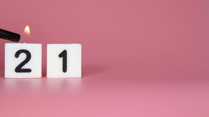 A square candle saying the number 21 being lit and blown out on a pink background celebrating a birthday or anniversary