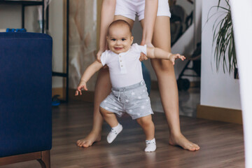 First steps of baby boy. Little child learning to walk. Mother helps her son to walk