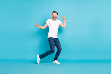 Fototapeta na wymiar Full body portrait of cheerful excited young person raise hands fists open mouth smile isolated on blue color background
