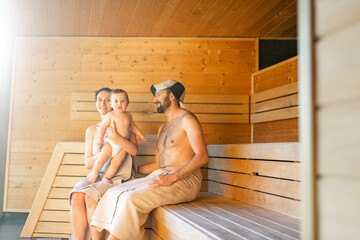 Young family resting with a little baby boy in sauna. Family vacation with one year child in spa