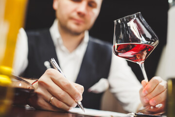Man fills in paper form holding delicious red wine at table