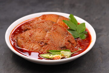 Seer Fish curry, traditional Indian fish curry ,kerala special ,arranged in a white bowl garnished with curry leaves and fresh  chilli on a grey textured background,isolated.