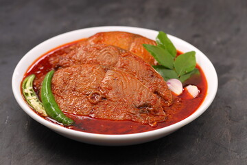 Seer Fish curry, traditional Indian fish curry ,kerala special ,arranged in a white bowl garnished with curry leaves and fresh  chilli on a grey textured background,isolated.