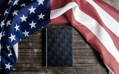 Obraz premium United States of America flag. Black book on a wooden background. Constitution. Guarantee of democracy.