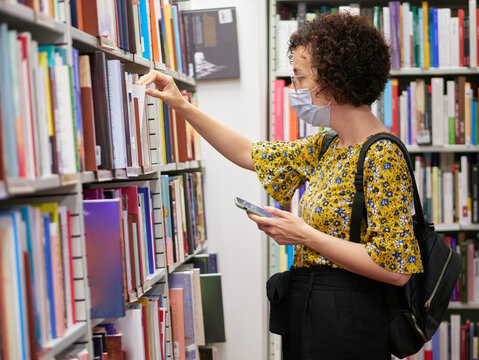 A Woman Looking At Books In A Bookstore Wears A Face Mask