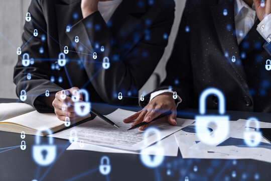 Two businesswomen working on the project to protect cyber security of international company. Padlock Hologram icons over the table with documents.