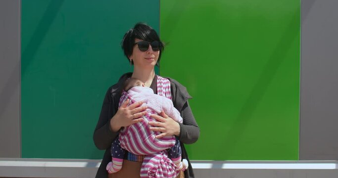 Woman posing, she uses a sling on the body. Securing the child nearby, natural parenting. Calmness of the kid on a walk. Green background.