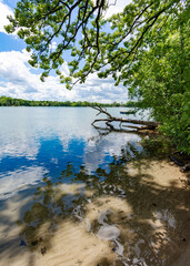 A vertical crop of a Wisconsin Lake (Lower Genesee Lake in Waukesha County).  A swimming raft floats on the calm waters while cumuls clouds are reflected.