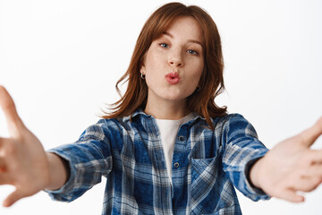 Tender and cute redhead woman kissing you, reaching hands to hold and hug someone, pucker lips, standing in plaid shirt against white background