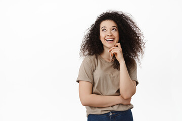 Portrait of stylish young woman laughing, smiling with white teeth and looking happy at upper left corner, standing in t-shirt against white background