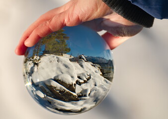 Russia. South of Western Siberia, Mountain Altai. View of the snow-covered rocky shore of Lake Teletskoye near the village of Yaylyu through a glass ball of perfect shape and transparency.