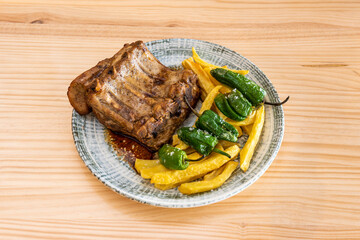 Semi overhead view of delicious roasted pork ribs garnished with homemade french fries, Spanish padron peppers and salt flakes