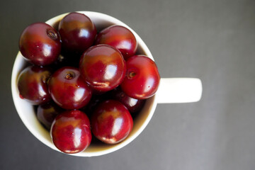 close red juicy cherry in a white cup on a dark background top view. ripe summer berries