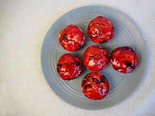 Six gluten-free muffins with rice flour cherries drizzled with cherries and red syrup stand on a gray plate on a beige tablecloth top view. homemade gluten free baked goods