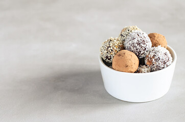Raw vegan dessert energy balls with hazelnut on a gray background. Natural sweets from nuts and dried fruits in coconut, cocoa and sesame seeds, close-up. Sugar-free and gluten-free sweets, raw food