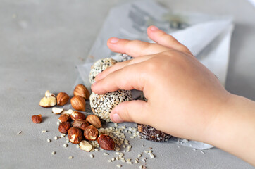 The child holds in his hand the Energy Bols - homemad raw, vegan candy. Mixed dates, nuts, dried fruits, sprinkled with coconut, cocoa and sesame seeds. The concept of healthy sweets. Paleo, keto diet
