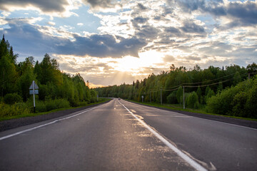 Fototapeta premium Country road with markings in the middle of the forest. Path and forward movement in the sun. Beautiful, green forest in the spring at sunset. Concept for success in the future goal and passing time
