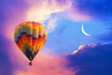 Hot air balloon flying in colorful evening sky with new moon shining