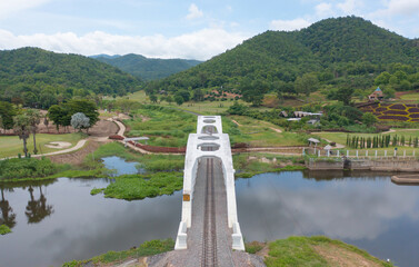 Aerial top view of Tha Chomphu White Bridge, Lamphun, Thailand with lake or river, forest trees and...