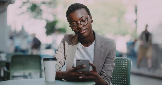 Young contemporary woman in business outfit sitting at table outdoor restaurant using mobile phone internat applications resting from work. Office break.
