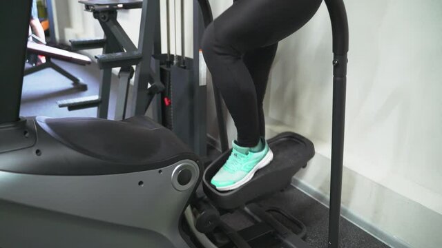 A brunette woman in the gym trains on a stepper in a black tracksuit and sneakers. Performs aerobic cardio exercise for weight loss. Fat burning