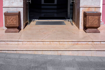 granite threshold with steps at the entrance to the store with a foot mat and stone trash can pots at the facade of the building close-up front view, nobody.