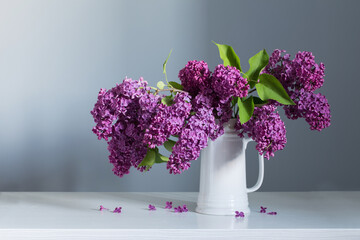beautiful lilac flowers in white jug on white wooden table