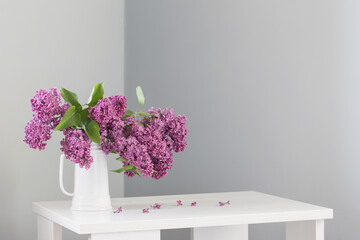 beautiful lilac flowers in white jug on white wooden table