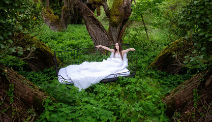sexy, cute, woman outdoors in bed, in white nightwear, in the nature magical fairy tale forest