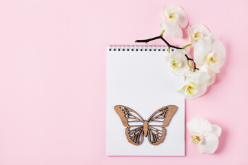 Open notebook and white orchid flowers on a pink background.