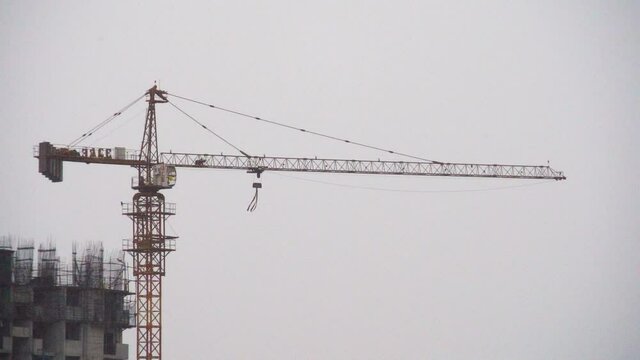 construction crane with long boom and strap hanging blowing in the wind in a thunder storm rain shower during a hurricane showing the bad weather the construction infrastructure real estate industry