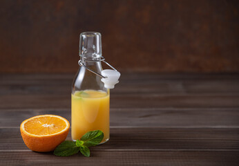 Fresh orange juice in bottle with citrus fruit and mint  on a brown wooden background. Rustic minimalism concept. Front view and copy space
