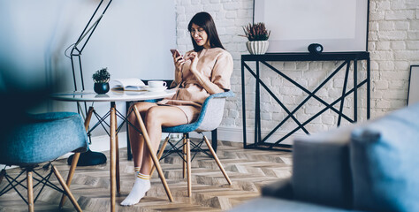 Pretty female blogger enjoying mobile messaging during leisure time in home apartment with good...
