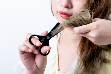 Close up images of Asian woman using scissors to trim and cut the ends of her hair, which is dry and damaged from changing hair color, to woman and hair care concept.