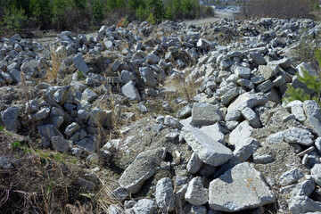 Heaps of dumped, gray, debris of concrete slabs and stones among the yellow, dry grass. Landfill for construction waste. Traces of an earthquake and a devastating catastrophe. Desolate area.
