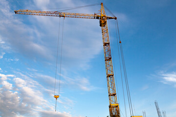 Tower crane of yellow color at a construction site against the background of the sky, bottom view.