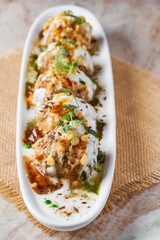 Chaat Dahi vada (AKA Dahi Bhalla, Doi Bora,  mosaru vade, Dahi Bara, thayir vadai, perugu vada ). Prepared by soaking vadas in thick dahi/curd (yogurt). Garnished with cumin and green fresh coriander