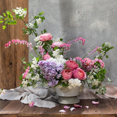 still life with summer flowers with roses and lilacs on a gray background in a vase