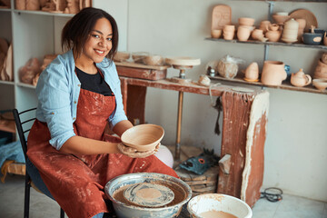 Joyful young woman ceramist working in pottery workshop