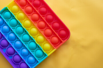 A rainbow toy lies against a background of yellow fabric. Blue and Orange Funny Interactive Anti-Stress Silicone Toys. Pop it