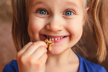 Naklejka premium Little girl holding nuts near her mouth. Child smiles and eats walnut.